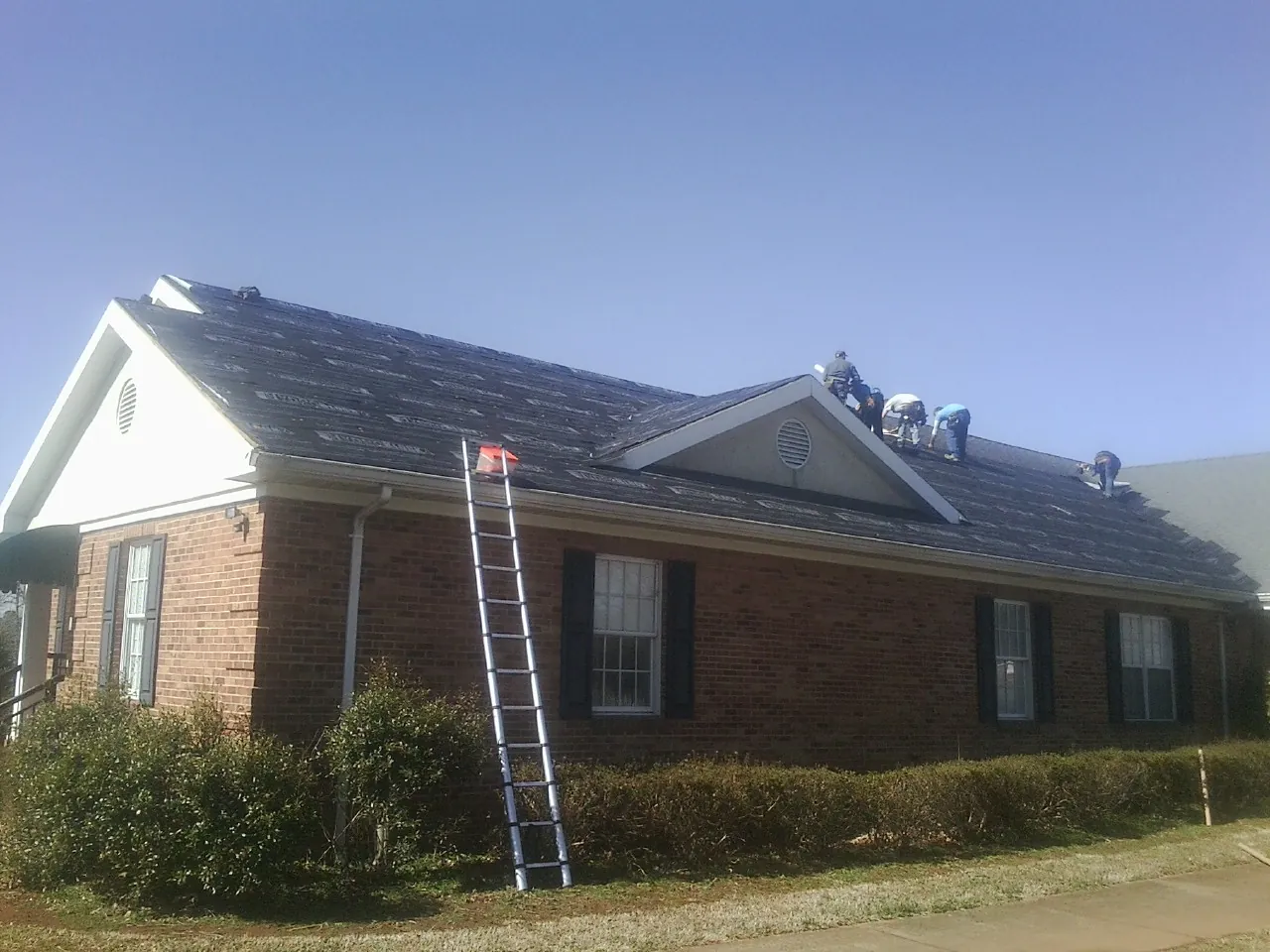 Crew tearing shingles off a brick ranch roof with a ladder set — Emergency Roof Repair work by our crew in Northvale