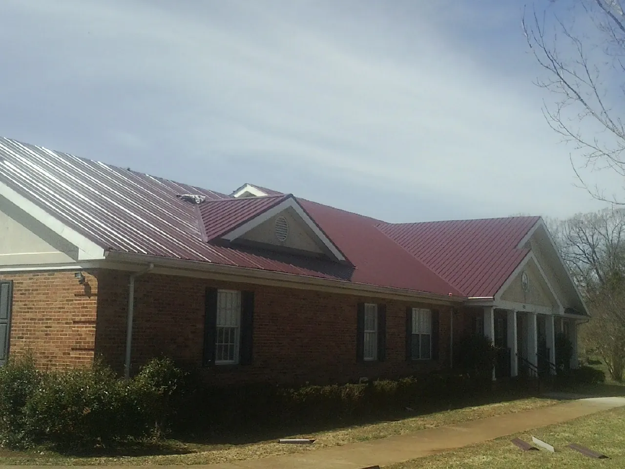 Red metal roof with gabled entries on a long brick building, from a Hail Damage Roof Repair job in Northvale