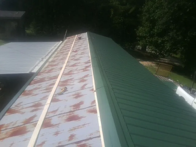 Old rusted panels beside newly installed green metal roofing — Wind Damage Roof Repair by Roofing Brothers in Northvale