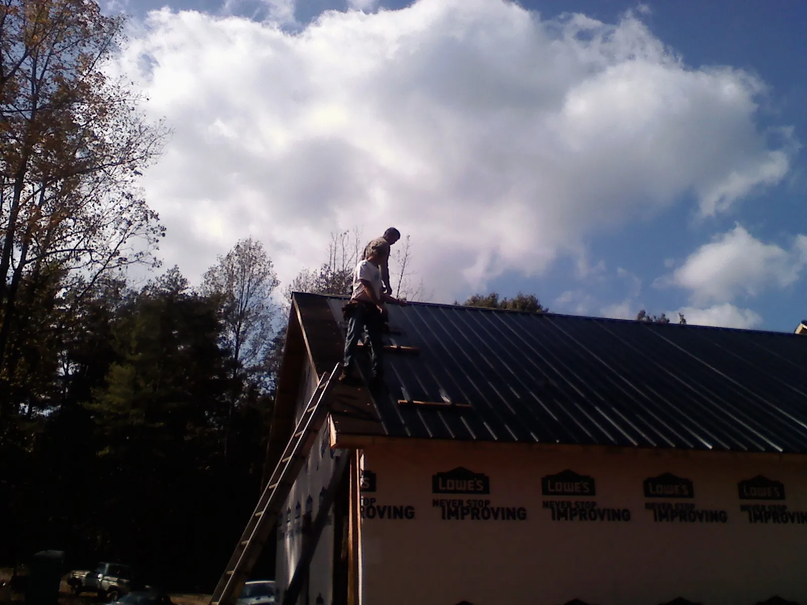 Roofer fastening dark metal panels high against a cloudy sky, from a Roof Inspection job in Northvale
