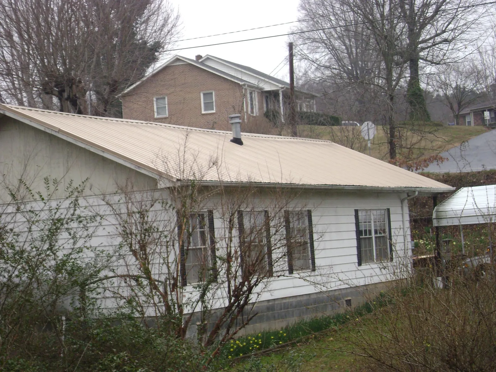 Tan metal roof on a white sided house set into a hillside — Commercial Roofing by Roofing Brothers in Northvale